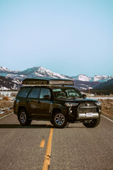 Black Toyota 4Runner with iKamper rooftop tent on a scenic road in snowy Montana mountains, perfect for an RV rental adventure.
