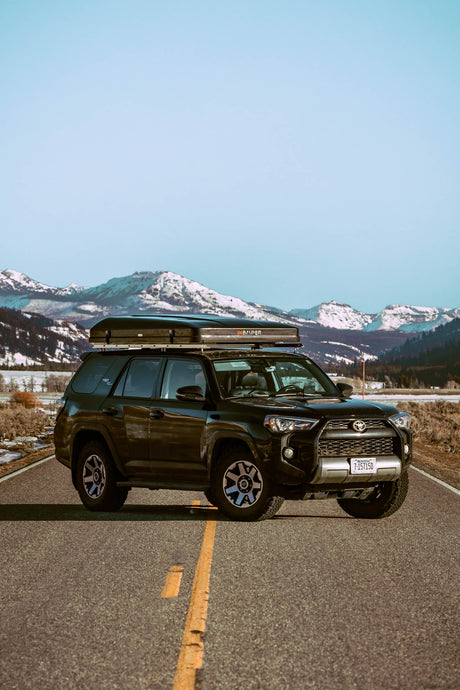 Black Toyota 4Runner with iKamper rooftop tent on a scenic road in snowy Montana mountains, perfect for an RV rental adventure.
