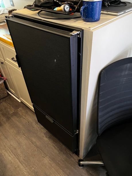Black portable fridge/freezer, partially open, with blue mug & electronics on top, in an rv rental setting. Practical RV living.