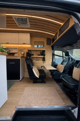 Modern RV rental van interior with wood panels. Features kitchen, dining table, and comfortable swivel seats for your next adventure.