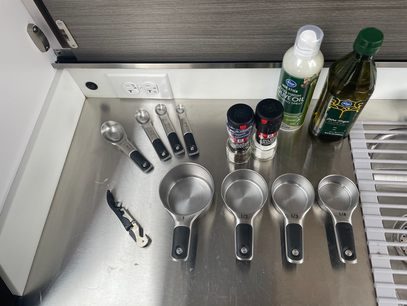 RV rental kitchen essentials: Measuring cups/spoons, oils, and spices on a compact stainless steel counter.
