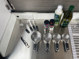 RV rental kitchen essentials: Measuring cups/spoons, oils, and spices on a compact stainless steel counter.
