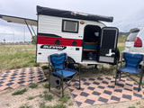 RV rental: A compact teardrop camper with an extended awning, camping chairs, and patterned mats awaits a relaxing stop.