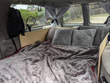 RV rental: Comfortable camper van bed with fluffy blankets, pillows, and charming string lights for a cozy night.