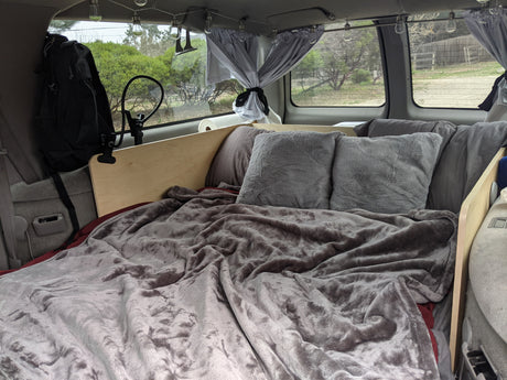 RV rental: Comfortable camper van bed with fluffy blankets, pillows, and charming string lights for a cozy night.