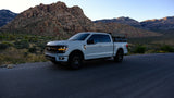 White Ford F-150 with rooftop tent for outdoor adventures, a unique alternative to an RV rental, set against desert mountains.