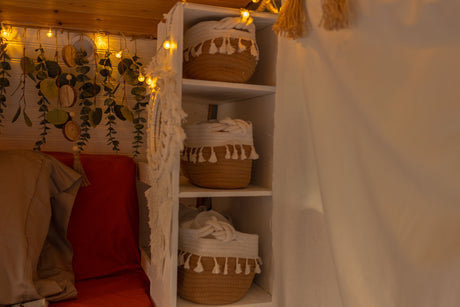 Inside a cozy RV rental: warm string lights, hanging greenery, a comfy bed, and clever storage baskets.