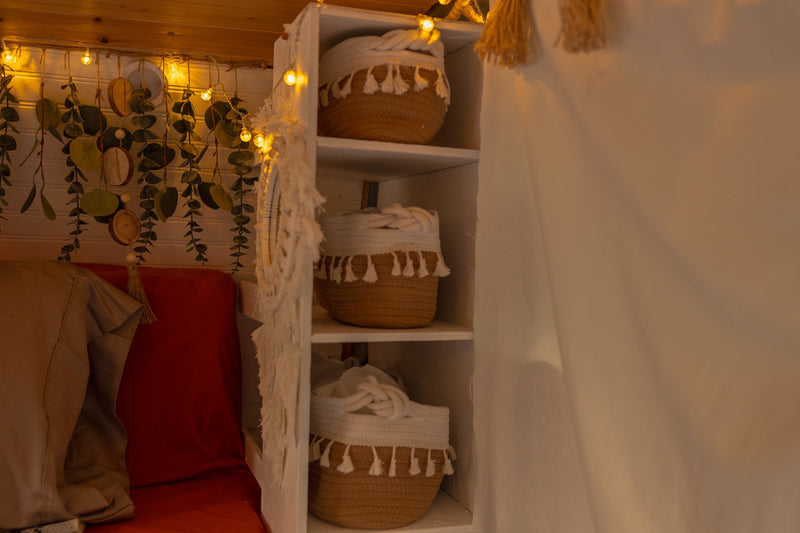 Inside a cozy RV rental: warm string lights, hanging greenery, a comfy bed, and clever storage baskets. — photo 15