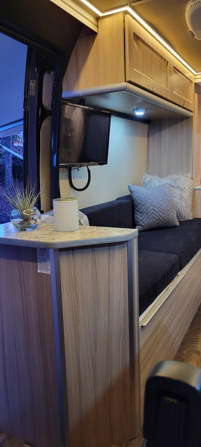 Experience comfort in this modern rv rental living space, featuring light wood cabinets, ambient lighting, TV, and a cozy sofa. — photo 14