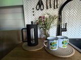 An rv rental kitchen view: fresh flowers, a French press, and "Adventure Awaits" mugs, all set on a cozy wooden counter.