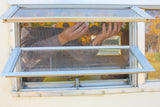 Through the screen of an RV rental window, hands are visible adjusting a colorful patterned item inside the vintage camper.