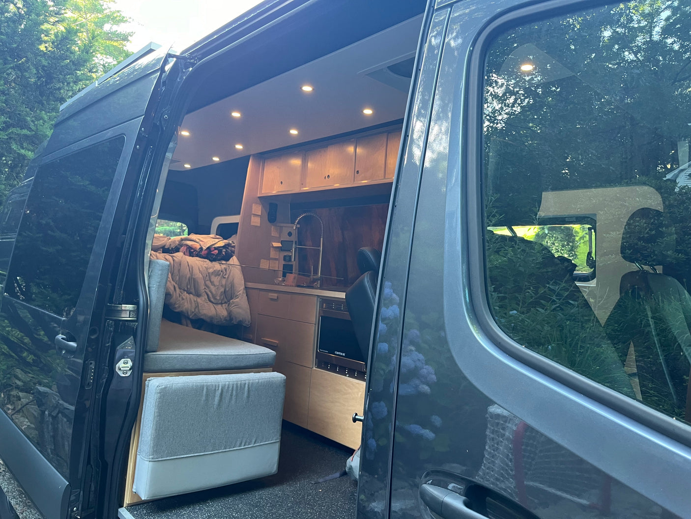 Modern RV rental camper van interior: open door shows kitchen, seating/bed area, and ceiling lights.