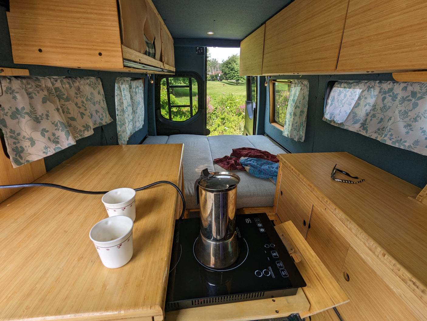 Inviting RV rental interior: bamboo counters, a portable cooktop, comfortable bed, and scenic view outside.