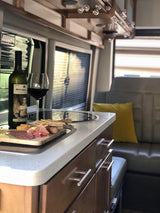 Cozy RV rental interior with wine, charcuterie board, and comfortable seating for glamping travel.