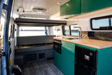 Spacious RV rental interior featuring a modern kitchen with green cabinets, comfortable seating, and an elevated bed.