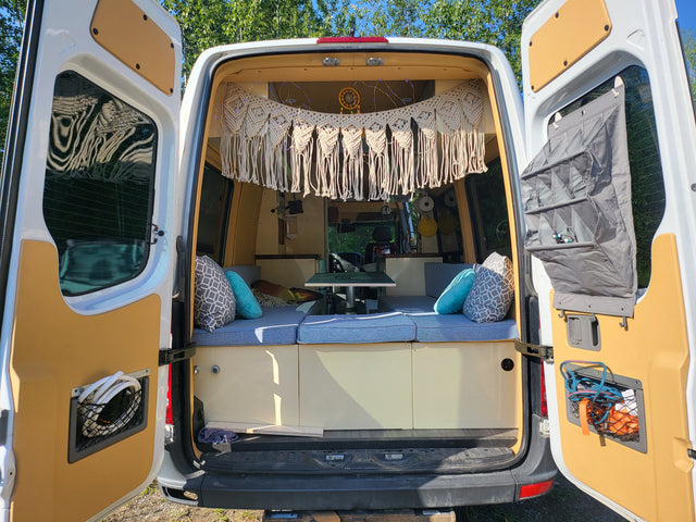 Step inside this cozy camper van RV rental, featuring blue seating, macrame decor, and smart storage for travel.