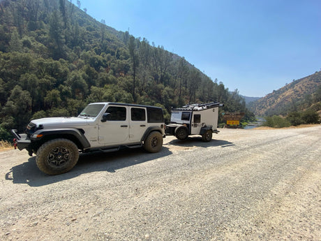 White Jeep and compact RV rental camper on a gravel road by the Merced Wild & Scenic River, perfect for off-road adventure.