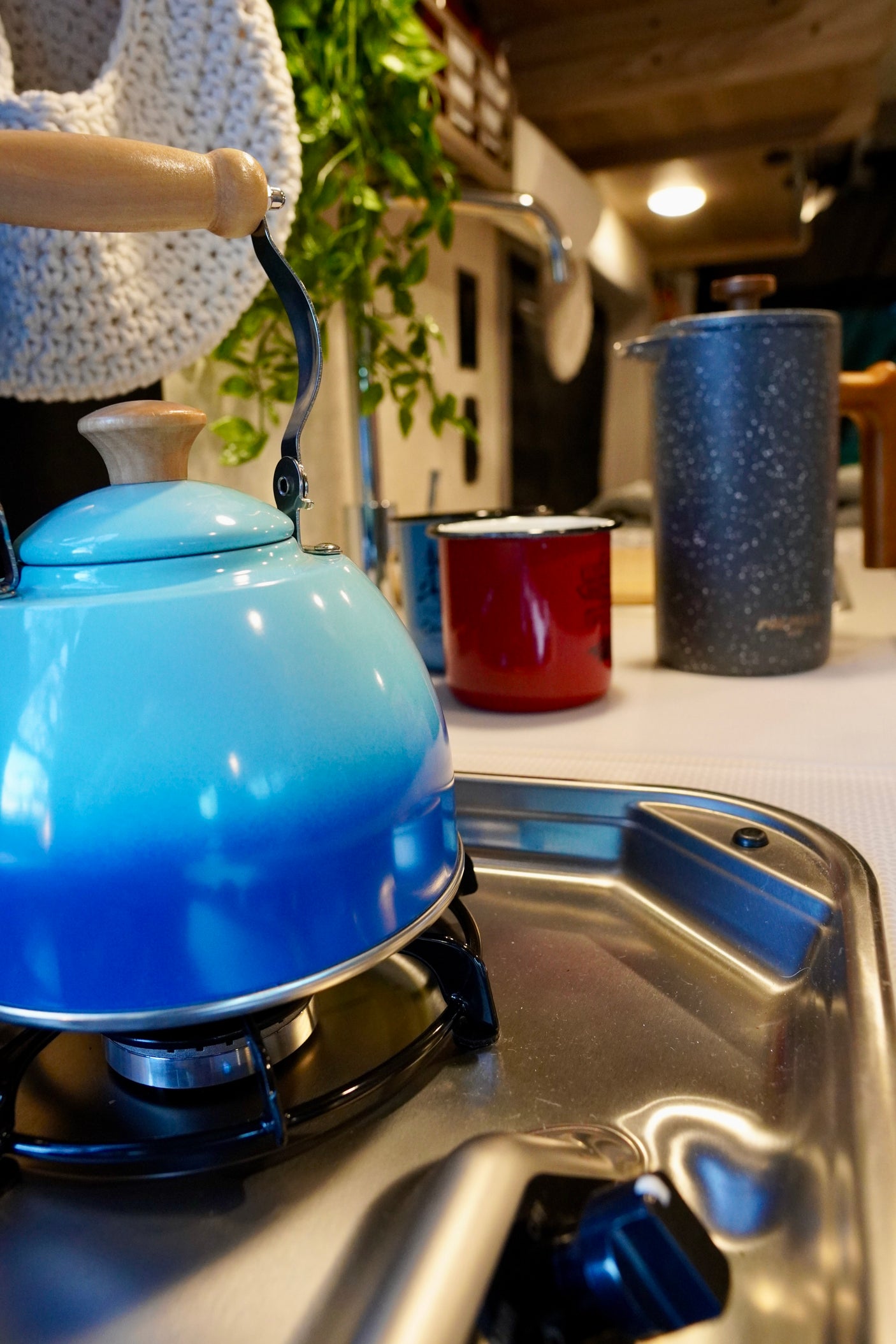 Compact RV rental kitchen with a blue kettle on the stove, perfect for camping trips.