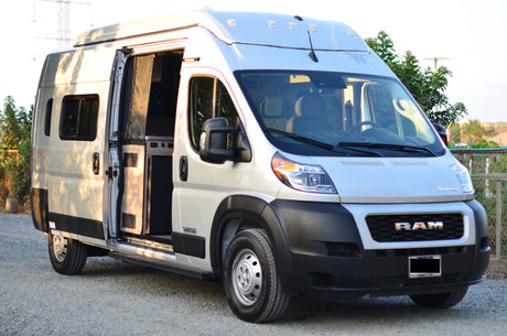 A white Ram ProMaster Winnebago camper van with open side door, showcasing its compact interior. Great for RV rental exploration.
