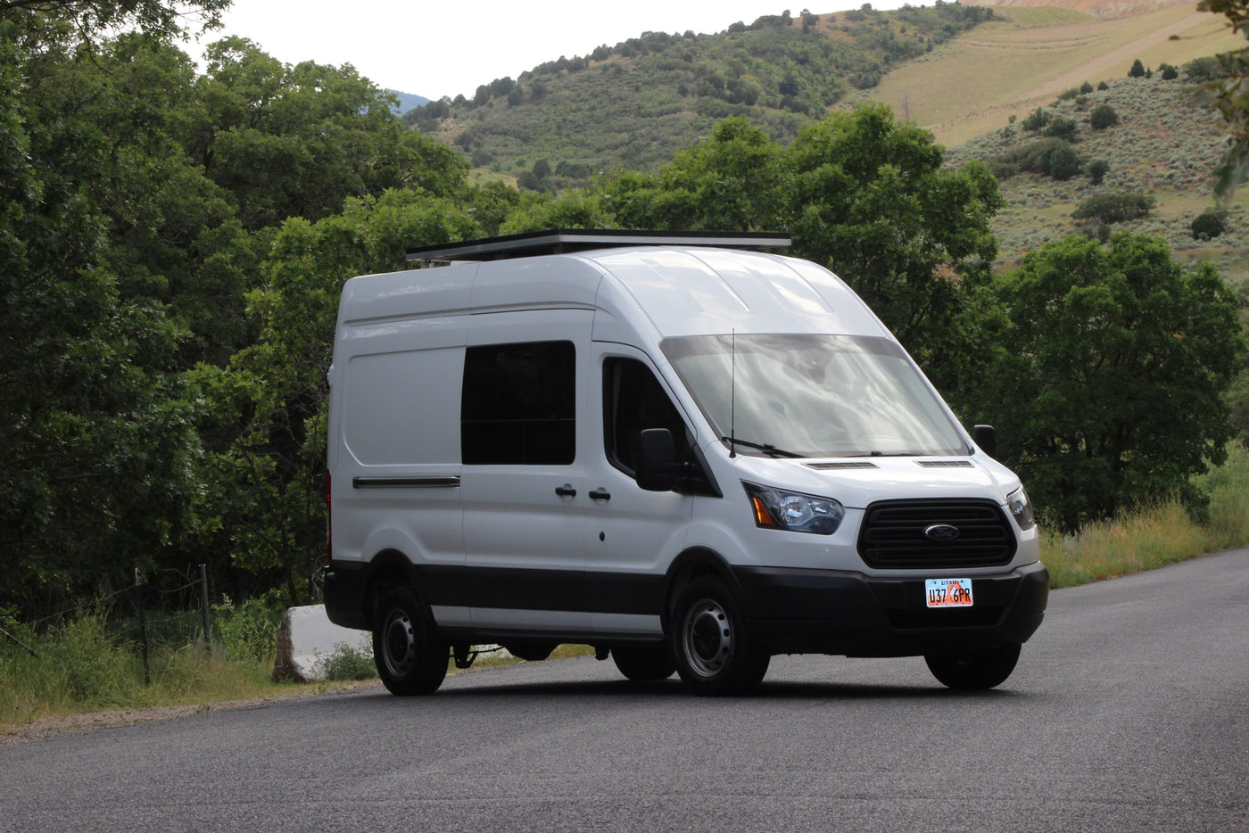 White Ford Transit camper van, ideal for RV rental, parked on a road with a scenic green mountain backdrop. — photo 9