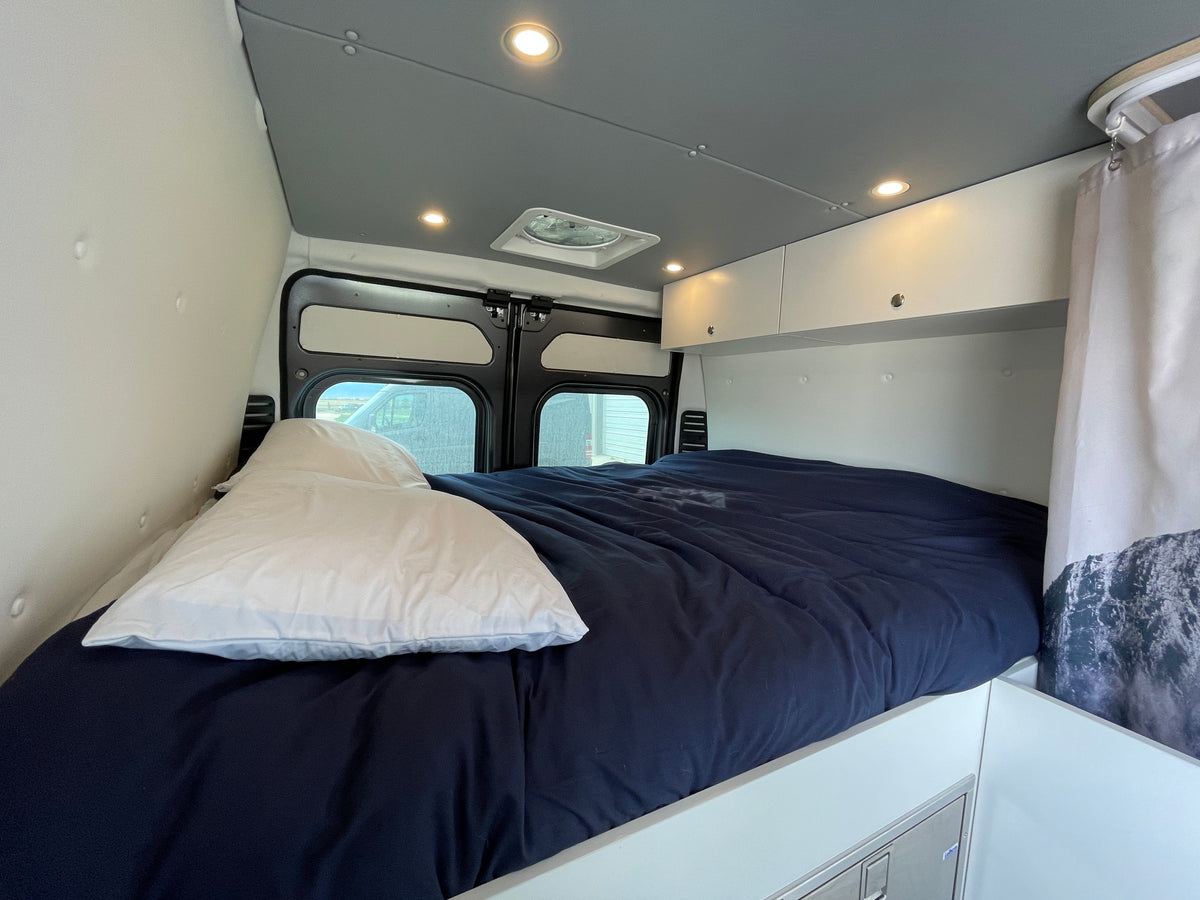 RV rental interior: A cozy bedroom with a dark blue bed, overhead storage, ambient lighting, and rear windows. — photo 19