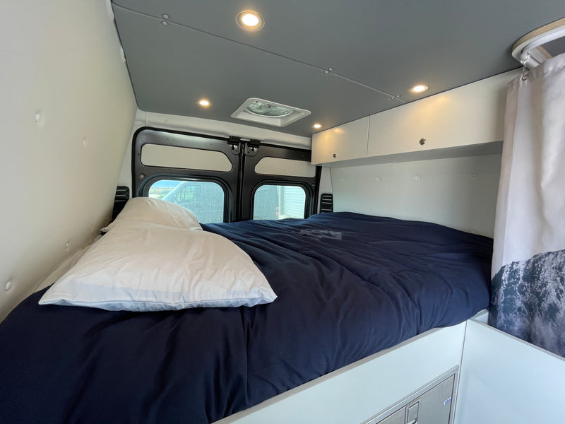 RV rental interior: A cozy bedroom with a dark blue bed, overhead storage, ambient lighting, and rear windows. — photo 19