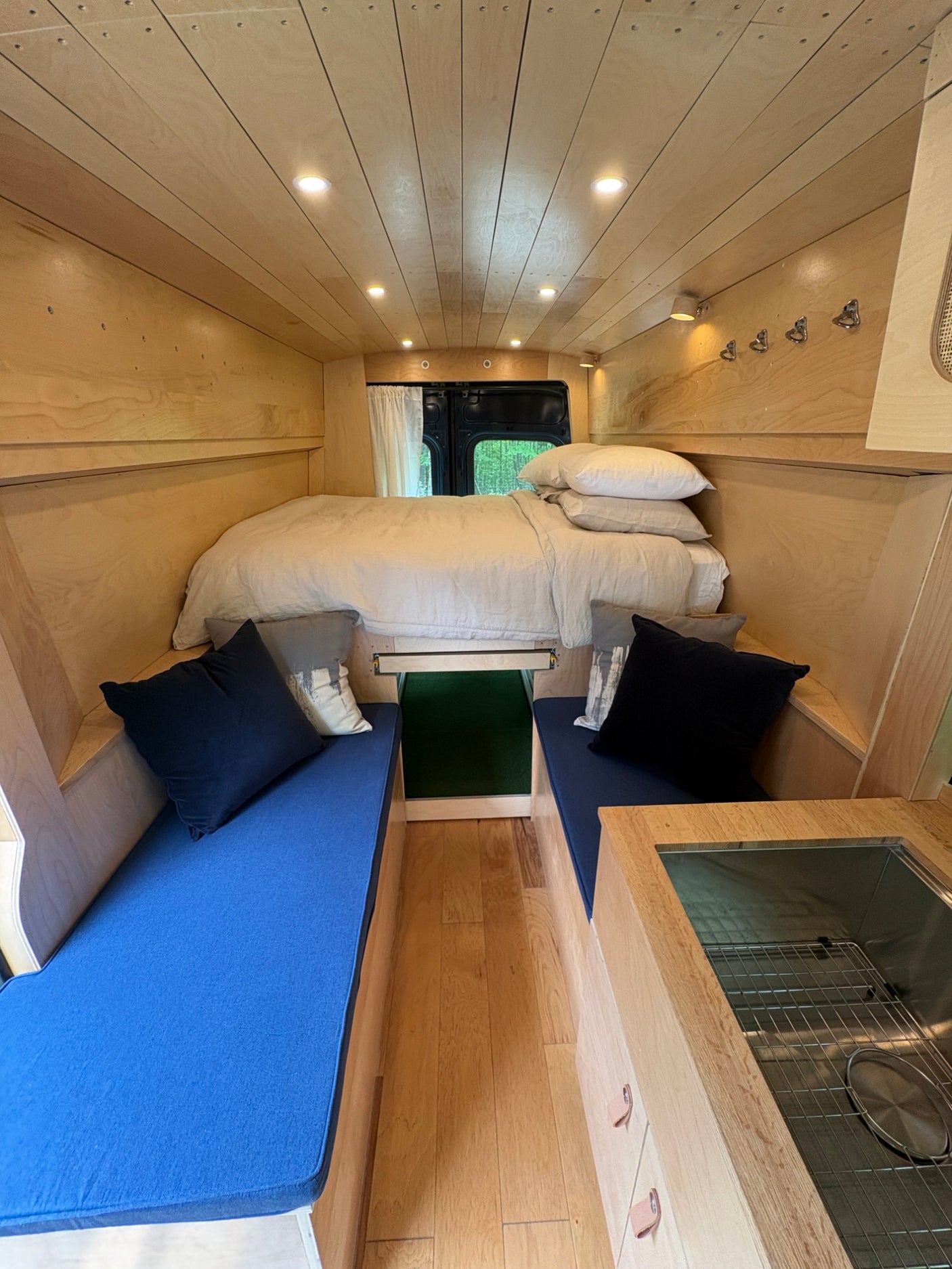 Step inside this cozy RV rental with natural wood walls, a comfy bed, blue cushions, and a functional kitchen sink.