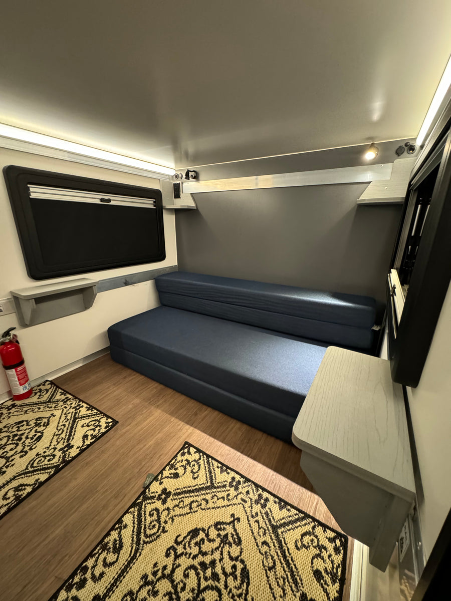 Bright rv rental interior features a blue convertible sofa, window, and wood floor with rugs. Compact & functional space.