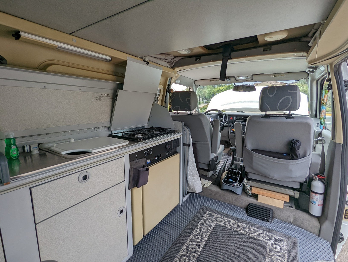 This RV rental's interior features a compact kitchenette (sink, stove, fridge), front seats, and pop-top roof. — photo 18
