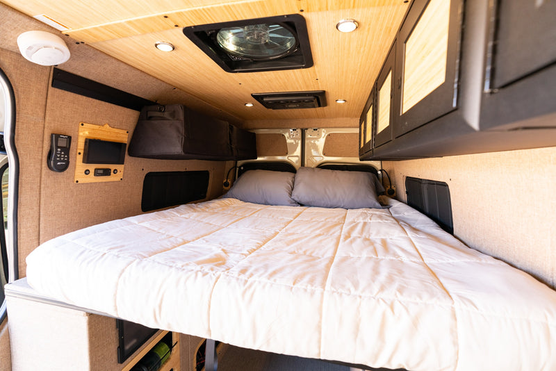 Cozy RV rental camper van interior with a large bed, wood ceiling, overhead storage, and essential controls on the wall. — photo 13