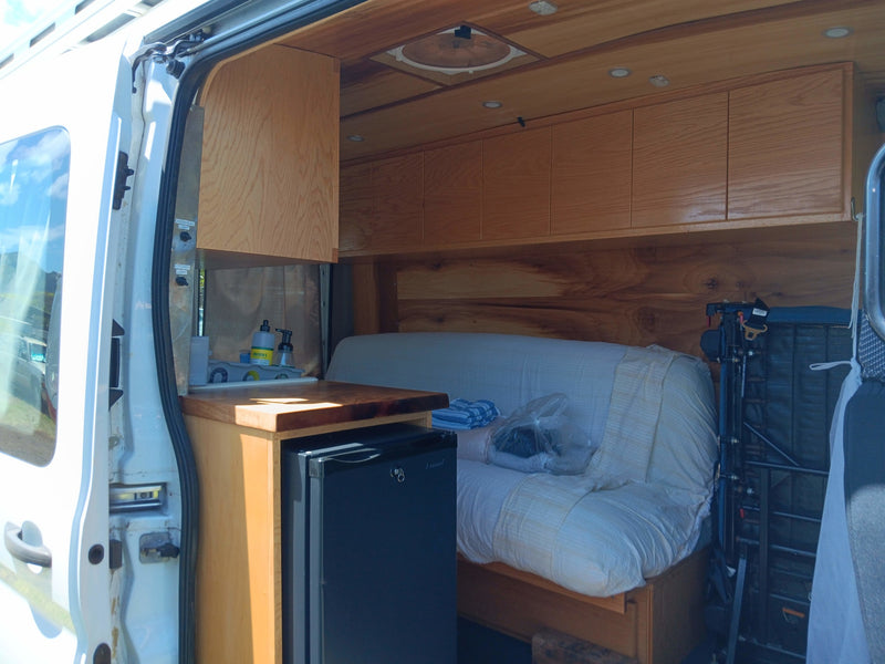 Cozy RV rental interior with custom wood cabinets, countertop kitchen, mini-fridge, and comfortable sofa bed. — photo 5