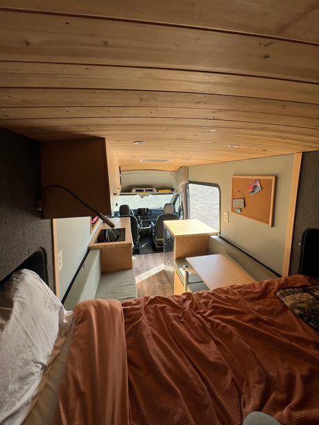 Explore this custom RV rental, featuring a comfortable bed, functional kitchen, and dining/lounge area, perfect for travel.