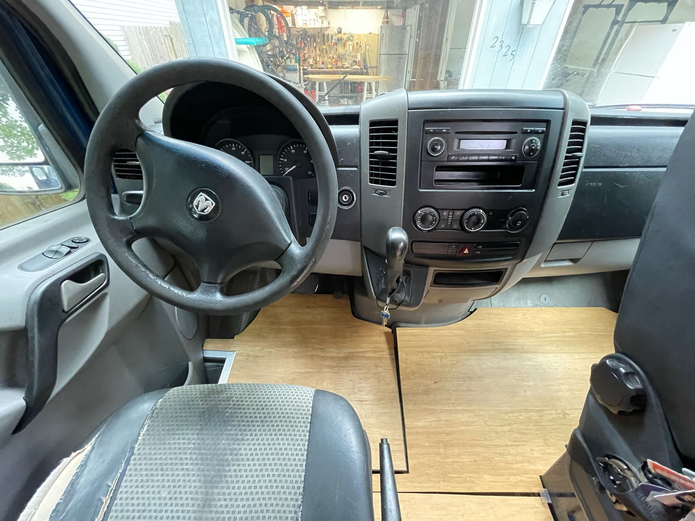 Interior of an RV rental: a converted van cabin with a wooden floor, steering wheel, and dashboard visible. — photo 11