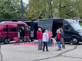Friends gather around two open camper vans, including an rv rental, with a dog and chairs. Ideal for group adventures.
