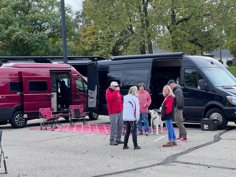 Friends gather around two open camper vans, including an rv rental, with a dog and chairs. Ideal for group adventures.