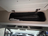Inside an rv rental or camper van, showing an open overhead storage compartment above the front dashboard.