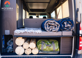 Organized RV rental campervan interior: storage with logs, gear, & comfy blankets for your next adventure.