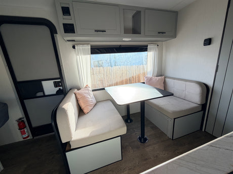 RV rental interior: A bright, modern dinette with comfy benches, table, and overhead storage, perfect for meals and relaxation on the road.