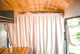 Interior of an RV rental camper van with wood ceiling, a light privacy curtain across the cabin, and storage.