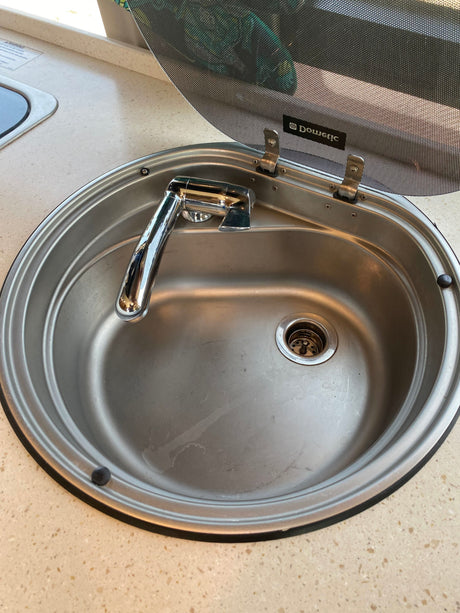 Stainless steel sink and faucet with an open Dometic glass lid, typical of an RV rental kitchen setup.