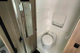 Compact RV rental bathroom: features a white toilet, integrated shower, and mirror.
