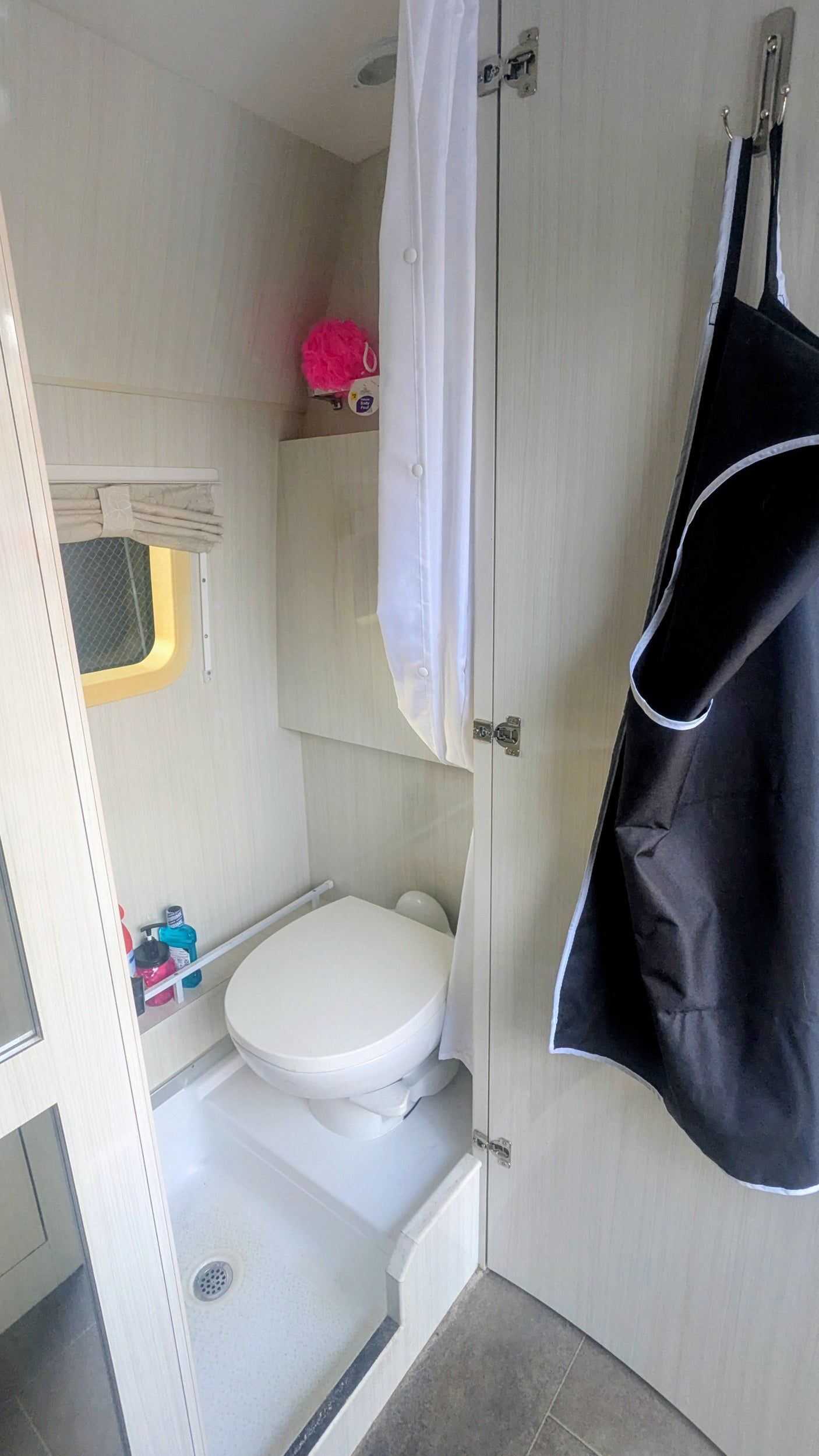 Compact RV rental wet bath featuring a toilet, shower pan, white curtain, and small window with blind.