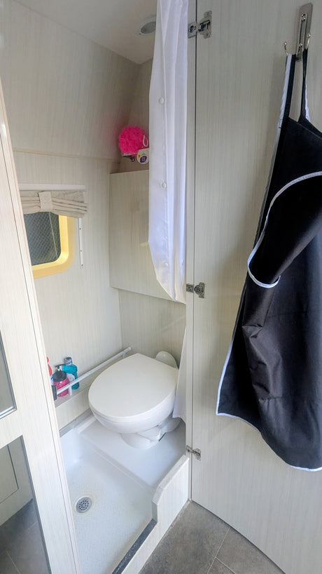 Compact RV rental wet bath featuring a toilet, shower pan, white curtain, and small window with blind.