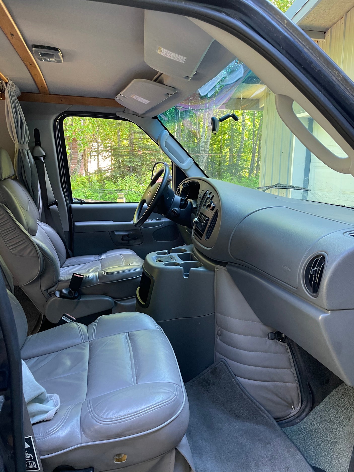 Inside a grey leather RV rental van, showcasing the driver's area, dashboard, and front windshield view of nature.