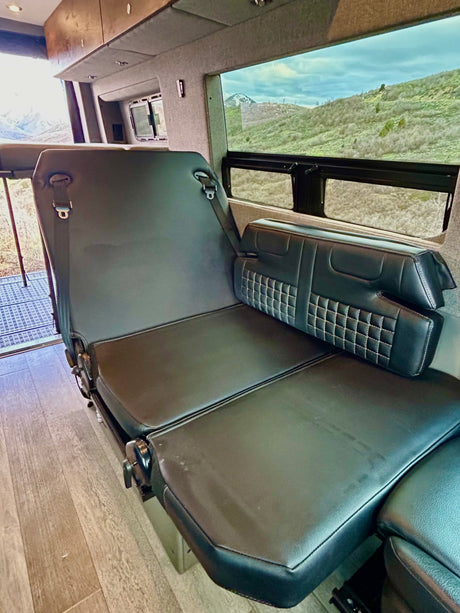 RV rental: comfy black leather van seat converts to a bed, ready for scenic mountain adventures.