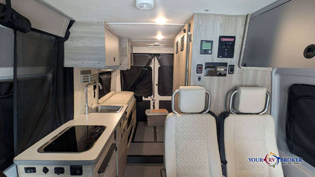 RV rental interior: Kitchenette with sink/cooktop, swiveling front seats, and control panel in a modern camper van living space.