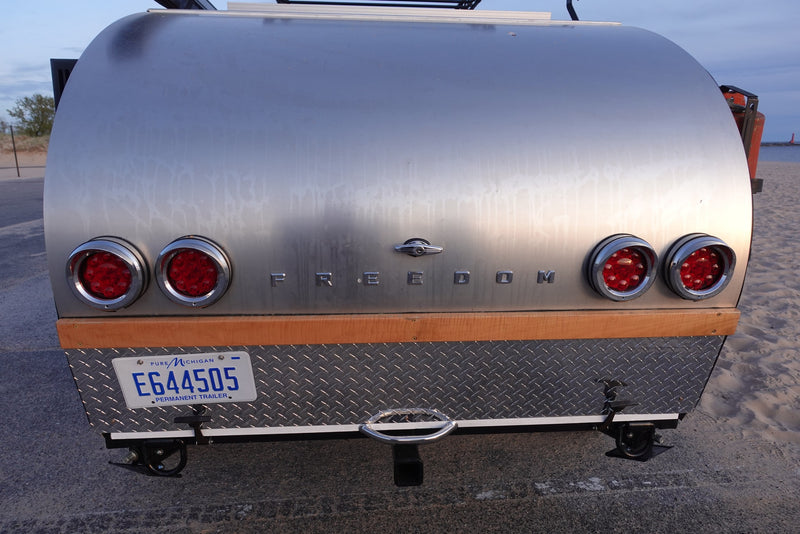 Rear view of a silver "Freedom" teardrop RV rental, Michigan plate E644505. Ready for adventure by the beach. — photo 15