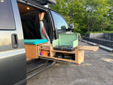 Open side door of an RV rental reveals a custom interior & a pull-out outdoor kitchen with a gas stove.