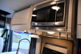 Stylish RV rental kitchen amenities: microwave, light-colored cabinets, glass shelf with under-cabinet lighting and paper towels.