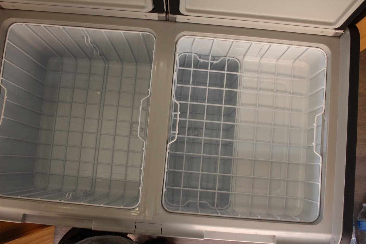 Clean, empty dual-zone portable refrigerator/freezer, ideal for your RV rental. Features white wire baskets for organized storage.